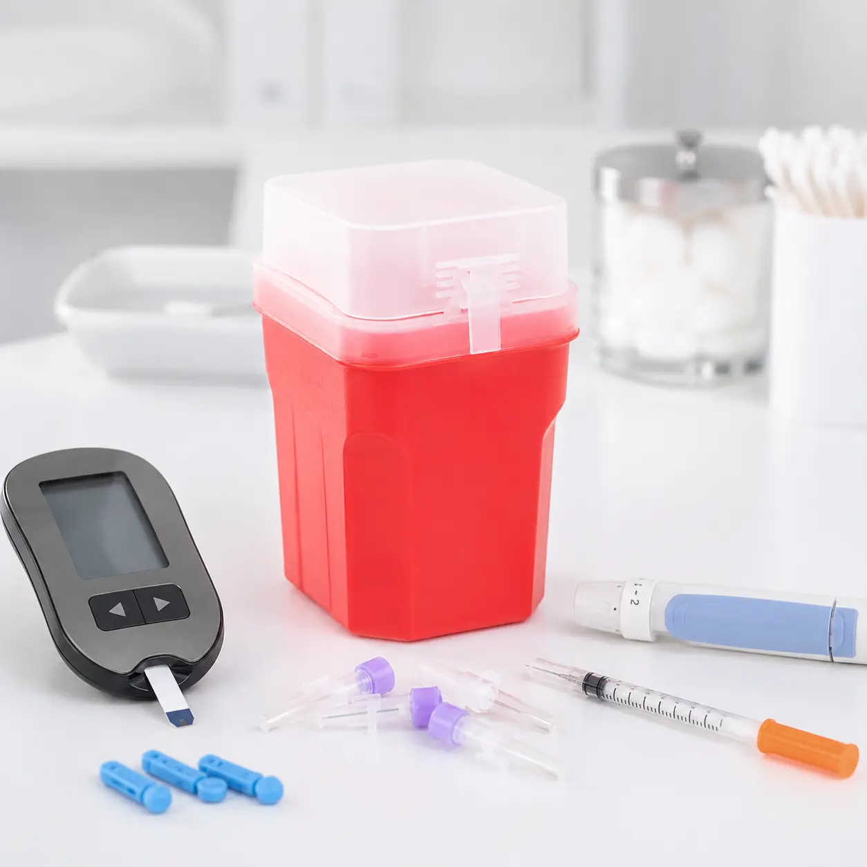Compact red sharps container shown with diabetes testing supplies and used sharps